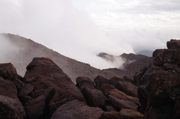 A photograph of rocks on a cliff oriented towards the Northeast, while further away lies a mist-covered slope.