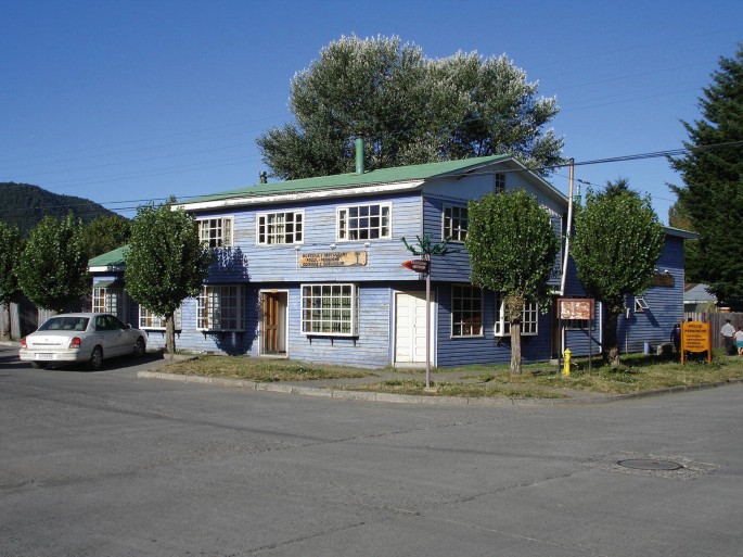 A photograph of a 2-story inn near the road with parking space, doors, and windows.