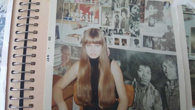 A photo presents the close-up of another photo in an album. It has a front profile of a woman seated on a chair against a backdrop of large posters.