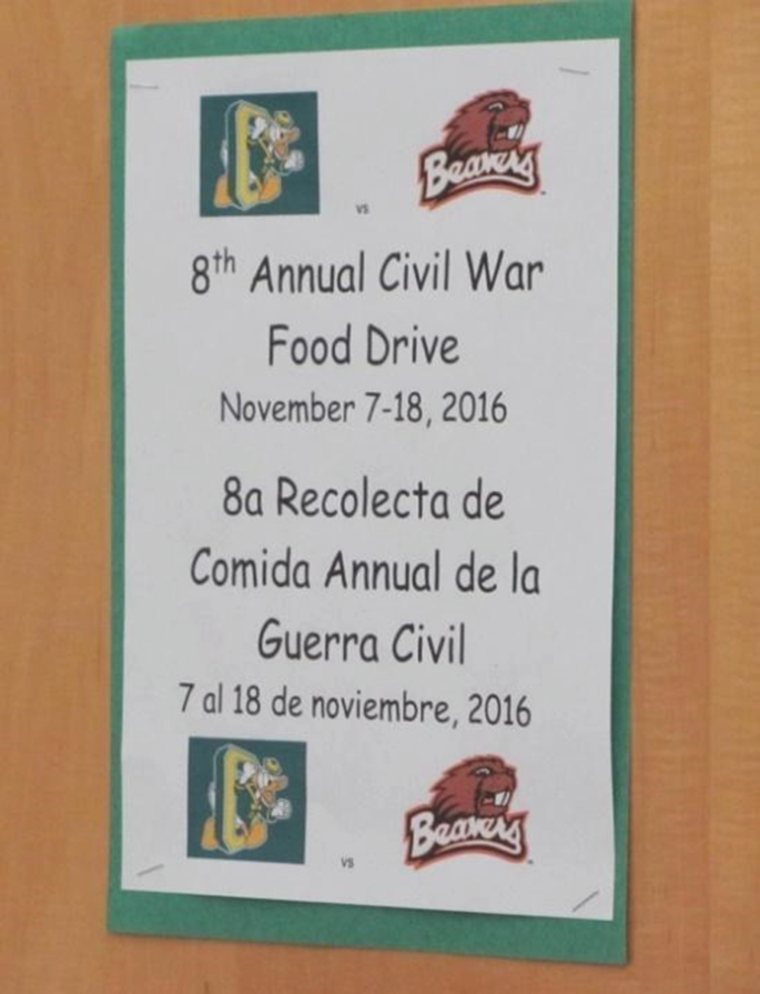 A photo of a poster pasted on a wooden door has text that reads, 8th annual civil war food drive, November 7 to 18, 2016. A translation in a foreign language appears below the English text. 2 logos of sports teams appear above the text.