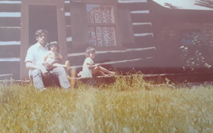 A photograph depicts a father and his two daughters sitting on the steps outside the house.