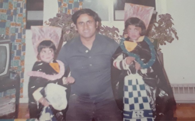 A photograph depicts a father holding his two daughters. The daughters are dressed up.