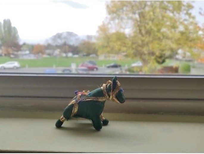 A photograph of a miniature toy horse wrapped in gold ribbon placed by a window.