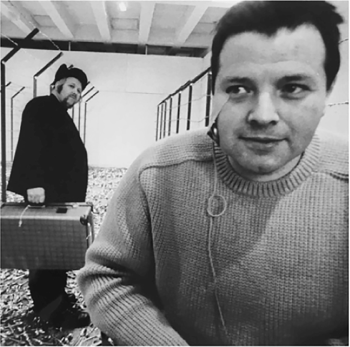 A photograph of Wolf Vostell and Helmut Rywelski. Rywelski has a microphone taped to his cheek.