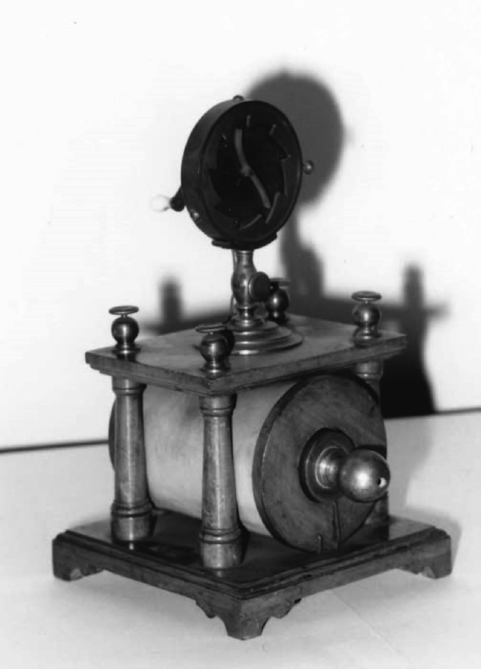 A historical photo of an induction apparatus featuring a cylindrical component surrounded by pillars on all four sides, topped with a measuring device.