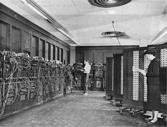 A vintage photograph of an E N I A C the first general-purpose electronic computer. A man and a woman standing with a book.