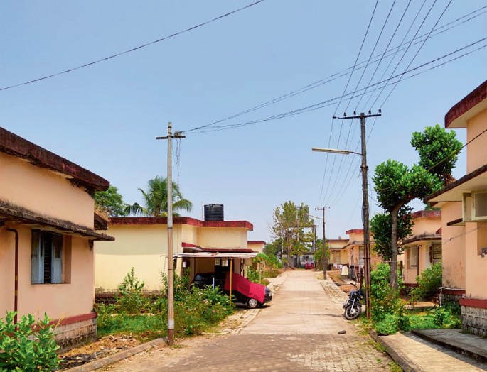 photograph of K E B Quarters features charming houses lining the sides of tree-adorned roads, with a backdrop of network poles. The central road adds a picturesque element.