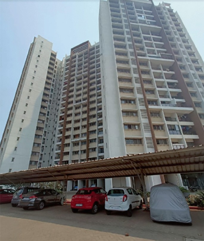 A photograph captures the grandeur of the multi-storey Raheja Waterfront Apartments, with a foreground exhibits a well-organized parking area filled with cars.
