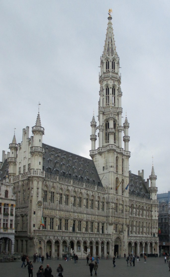 A photo of the town hall in Brussels presents a large building with a clock tower, ornate facades, and an openwork parapet crowning the facade.
