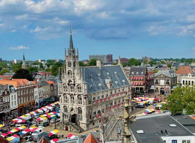A photo of the town hall in Gouda in the center of the market square. Numerous buildings and people surround the town hall.