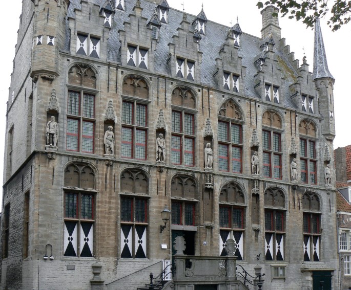 A photo of the town hall in Veere presents a tall building with architectural details. The facade alternates throughout with arched windows and statues.