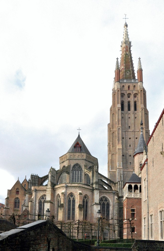 A photo of the tower of Our Lady in Bruges presents a large building with a clock tower.