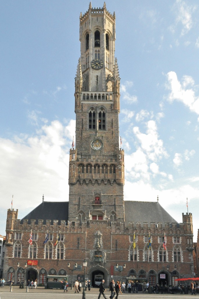 A photograph of the belfry of the cloth hall and the buildings attached to it. The photo presents the tower's facade, with a large arched doorway and several windows.
