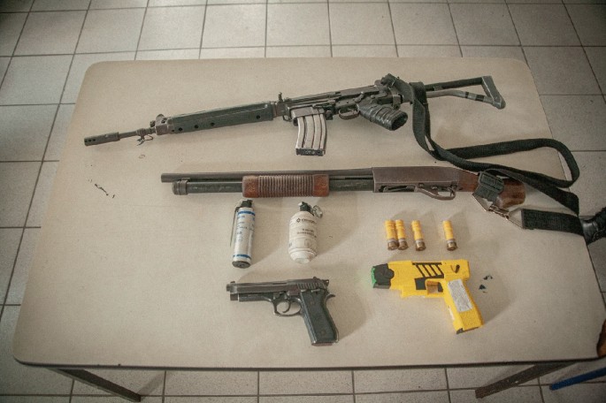 A photo of two rifles and two revolvers on a table along with bullets and two bottles.