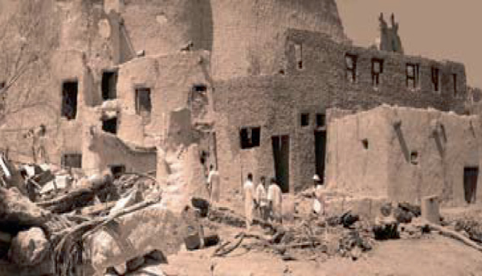 A photo of 3 men standing near demolished old Siwian houses.