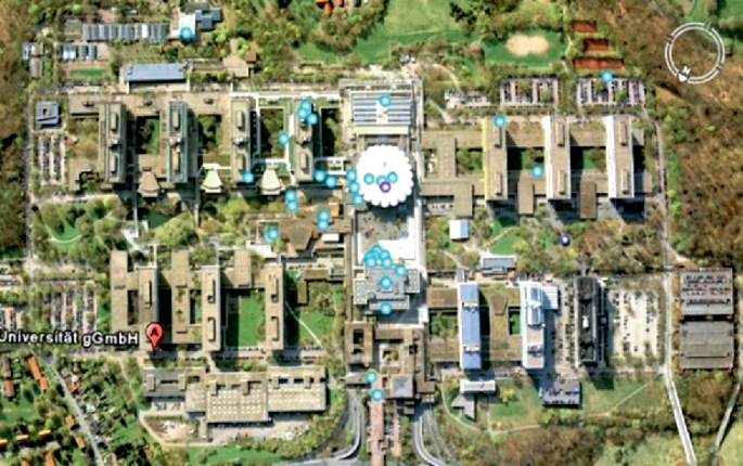 A satellite view of the Bochum University of Germany features its architectural layout and surrounding foliage. The layout consists of a main building with 7 and 6 smaller buildings at the top and bottom. There are patches of green areas, indicating lawns or gardens interspersed among the buildings.