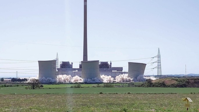 A photograph of a large power plant that emits smoke and is located on grassland.