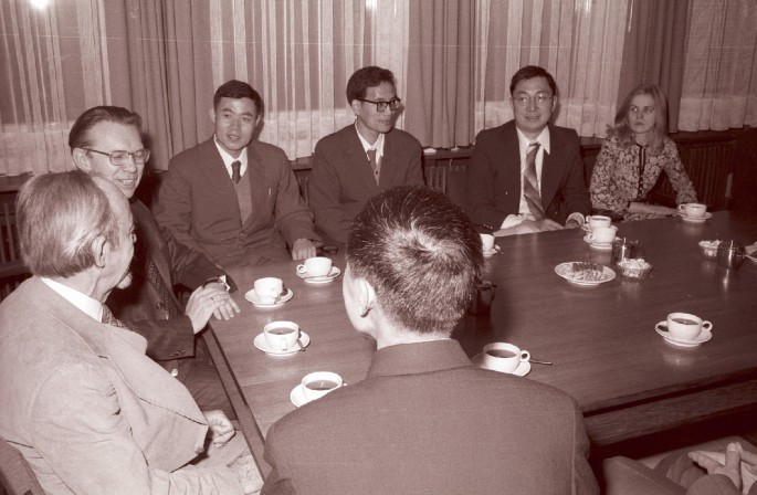 A photograph of Herwig sitting at a table with a Chinese delegation. Sam Ting is also seated at the table with his future wife Susan. There are tea cups on the table.