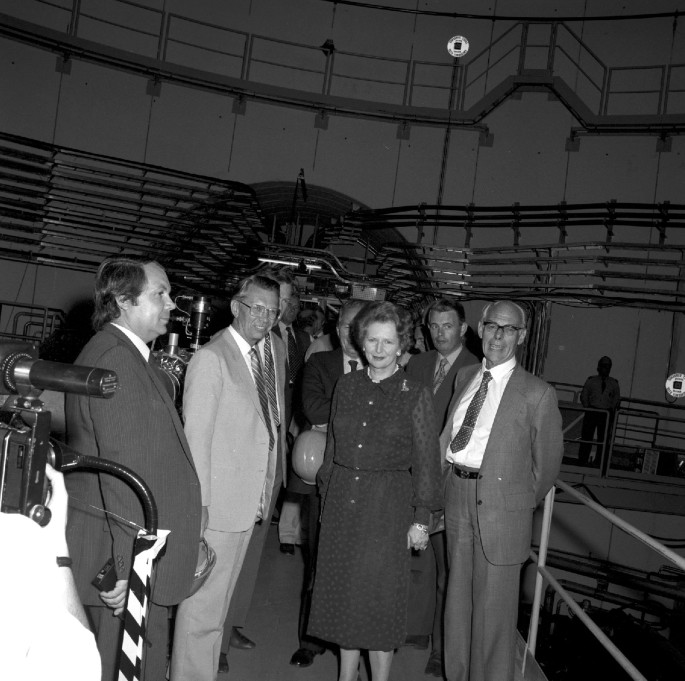 A monochrome photograph of Herwig with Margaret Thatcher and Denis Thatcher along with other people in an experiment laboratory.