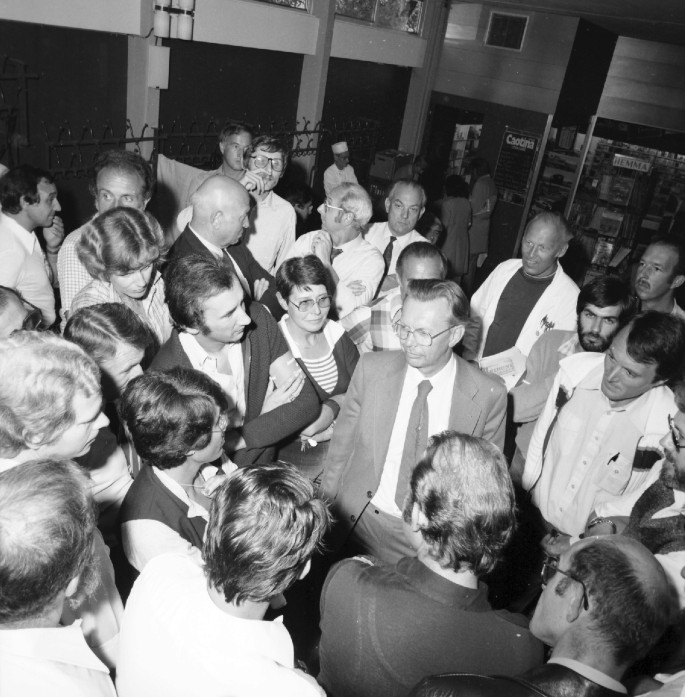 A photograph of Herwig surrounded by a group of people where Herwig discusses with the people.