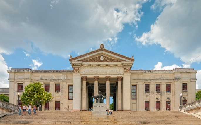 A photo of large 2-storied building. It has a central square structure with a slanting roof supported by 8 pillars. A flat-roofed structure extends on either side of it with 8 large windows each.