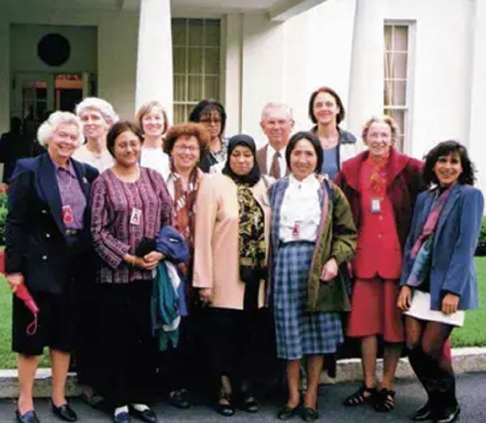 A group of 10 women and a man pose in front of a building. They stand in 2 overlapping rows.