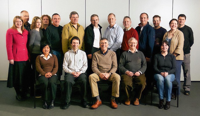 A photograph of a group of S P D O staff in 2011. Five people are seated, and other people are standing behind them.