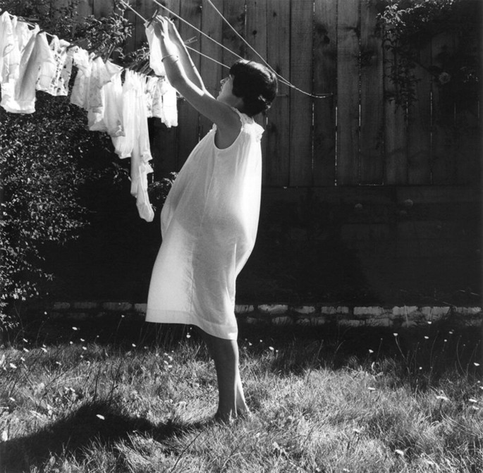 A photograph of women in white attire, drying clothes on a rope.