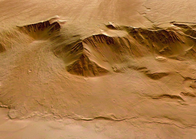 A photograph of the dusty surface of Olympus Mons. It displays an irregularly shaped pit on its surface.