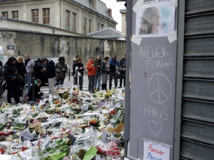 A photograph displays people offering flowers on the street. Texts written below a photo of a woman reads, never forget Paris.