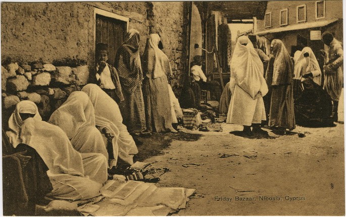 An old photograph of a group of women covered from head to toe in flowing robes. The stand in groups, or sit on the floor, near the entrance of a building.