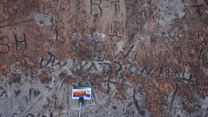 A photograph portrays a rock bearing inscriptions discovered at the Gray Rock historic graffiti site, accompanied by a card placed on the rock.
