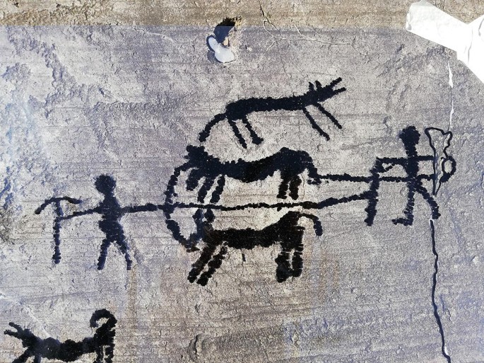 A photograph of a rock art representing two animals plowing the field.