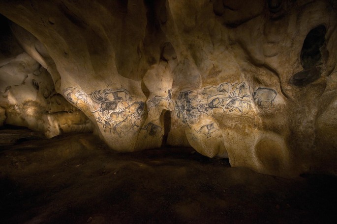 A photograph of the cave walls covered in ancient drawings and paintings, depicting various animals under studio lighting.