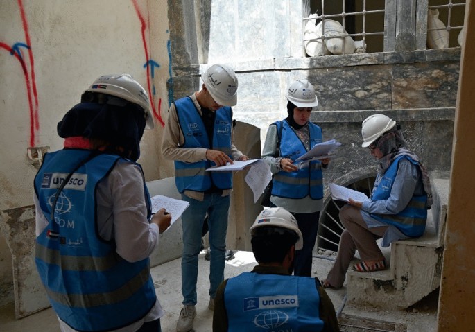 A group of construction workers in hard hats and vests, gathered around blueprints, discussing plans and reviewing documents.