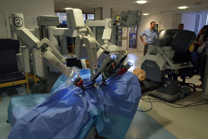 A photograph of surgical robots equipped with 3 arms. The robots performing the surgery of a dummy patient.
