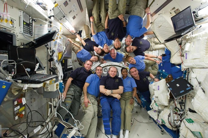 A photograph of 13 astronauts gathered in the International Space Station. Laptop-like devices and other equipment are installed there.