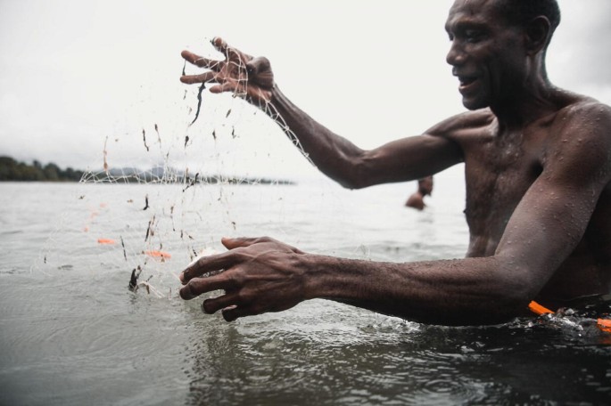 A photograph of a man cleaning his fish net in the water.