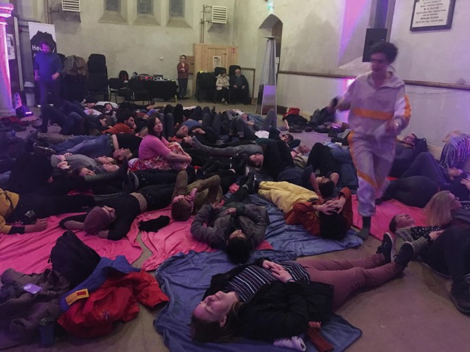 A photograph of a large group of people lying in a hall on their backs.