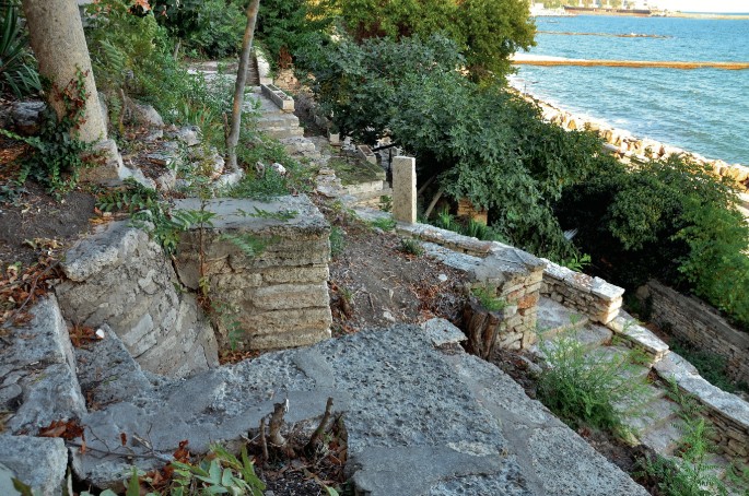A photograph of stone platforms and a stone staircase amongst trees, with a coastline in the background.