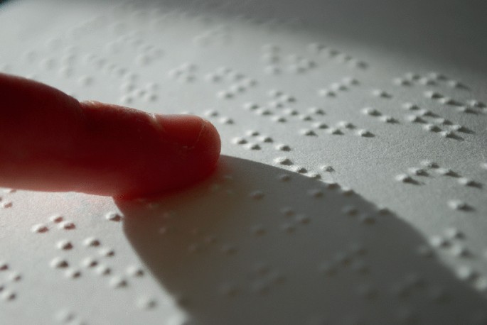 A photo of a Braille book with a finger touching the raised dots.