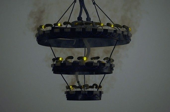 A photo of a dark chandelier hanging from the ceiling, emitting smoke from three sections.