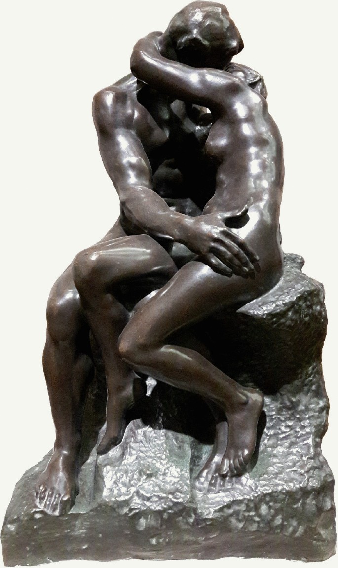 A bronze statue of a nude man and woman seated on a rock. The female figure leans against the man, holding him around the neck, while he holds her outer thigh.