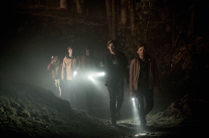 A snapshot of a scene from the series Dark displays four men and a woman holding torch in their hands in the dark.