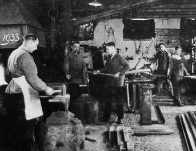 A monochrome photograph of some men working with tools in a room.