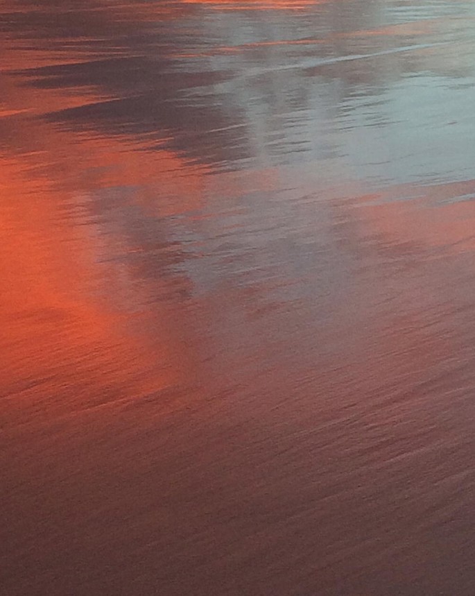 A photograph of the sunset reflected on the surface of a calm sea.