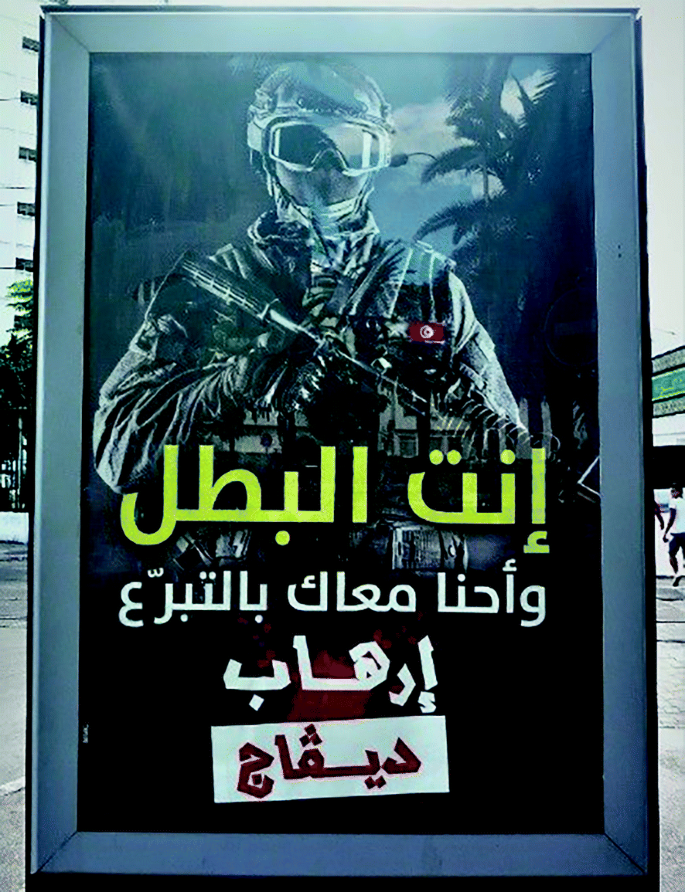 A photograph frame depicts an armed man wearing glass and holding a gun in his hand. The text on the frame is in Arabic.