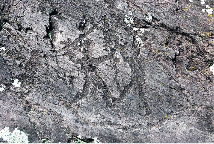A photograph of a top view of a rock surface, in Seradina. Three human figures with raised arms and weapons are engraved on them. They are facing each other and have long swords in their hands.