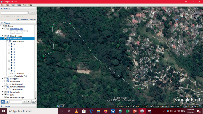 A screenshot of pipe network using google earth pro. The left pane displays the folders and drives. The right pane displays the image. It depicts a forest area and the nearby houses and buildings. The pipe network is drawn based on the G P S coordinates.