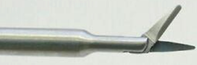 A picture of a medical instrument's tip. The base of the instrument is metallic, the appendage is small scissors, with one of the cutting edges placed higher than the other.